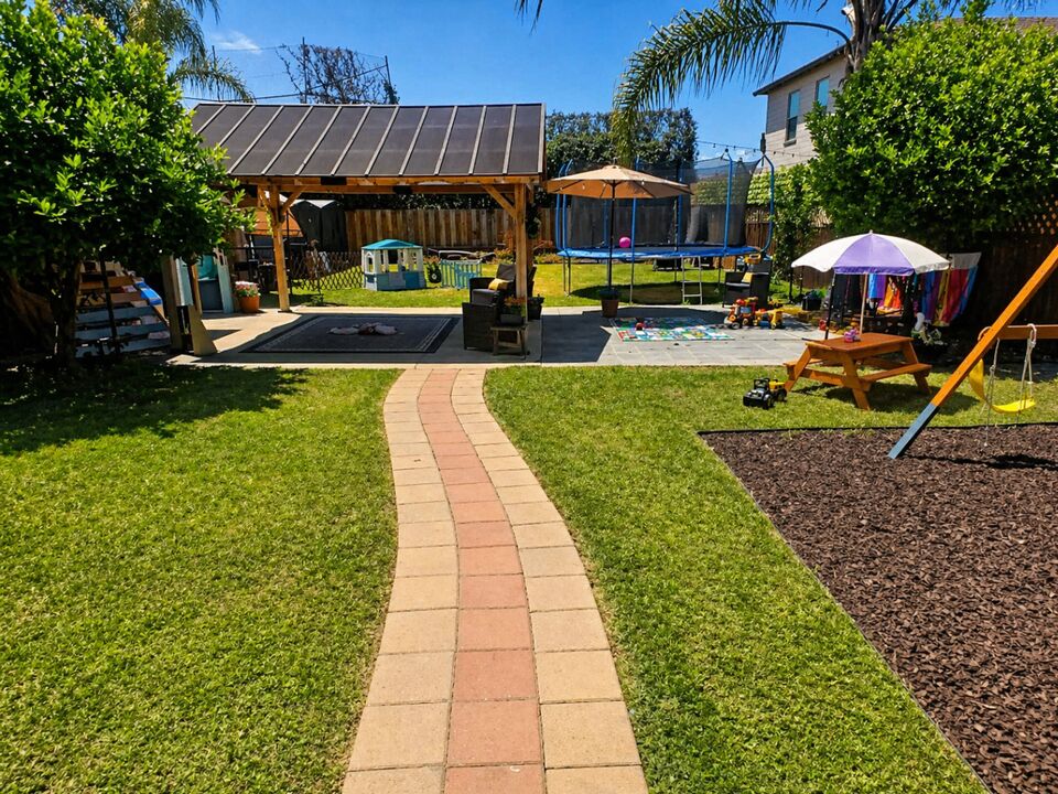 Spacious Happy Sprouts backyard with a covered play area, trampoline, and grass lawn