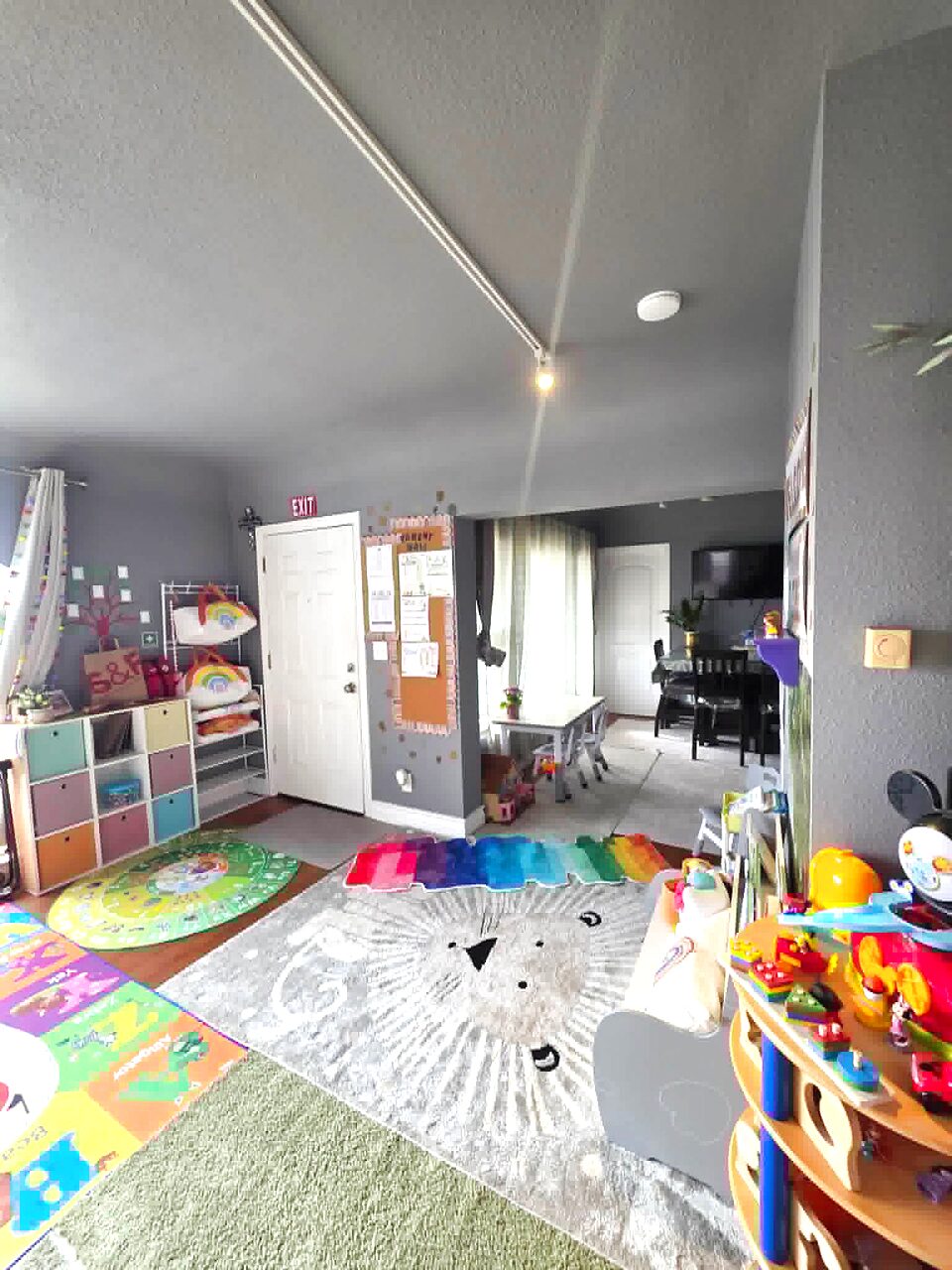Bright entryway at Happy Sprouts with rainbow rugs, lion play mat, and view through to the dining area