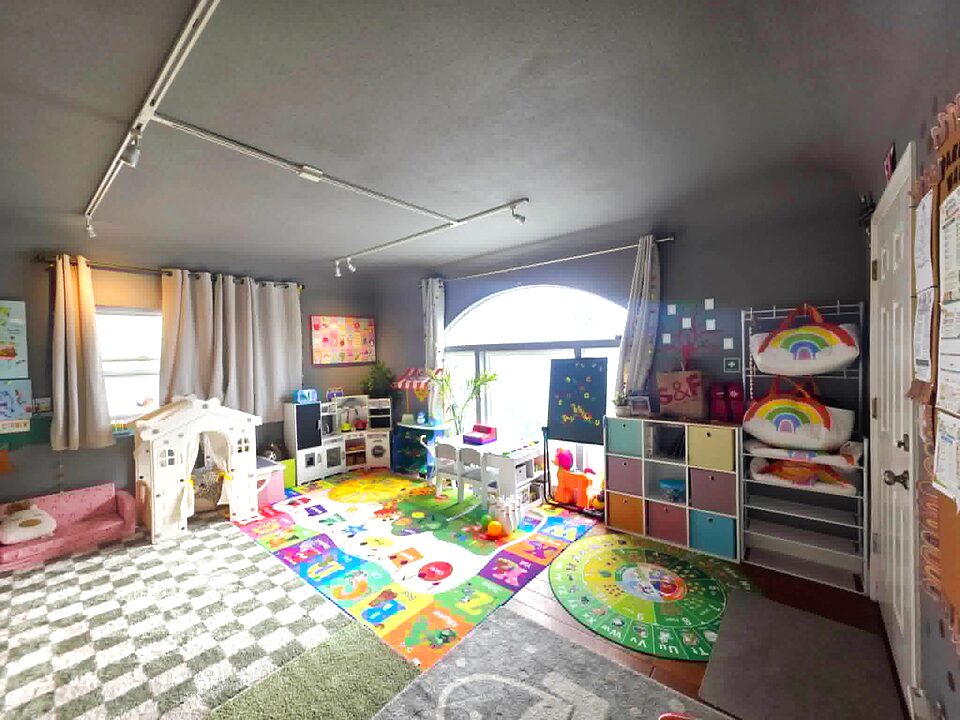 Open playroom at Happy Sprouts with alphabet rug, playhouse, kitchen set, and colorful cubby storage